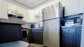 A modern kitchen with white and dark cabinets, a stainless steel refrigerator, a microwave, and a granite countertop.