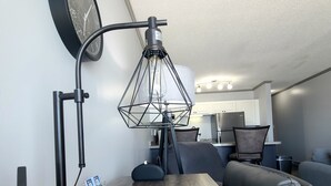 A modern living room with a wooden coffee table, a black desk lamp, a clock on the wall, and a kitchen area in the background.