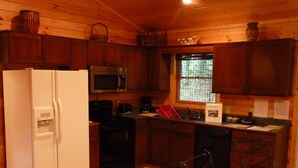 A compact kitchen with wooden cabinets, a white refrigerator, a microwave, a stove, and a sink. - Ralph's Place  6 Min to Downtown Immaculately Kept (Boone)