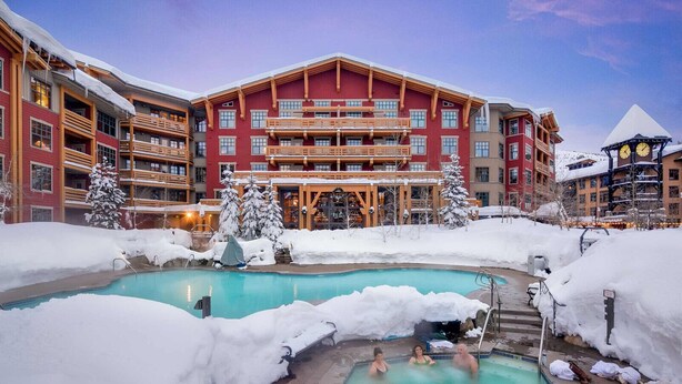 Un hôtel doté d’une piscine entourée de neige, avec de nombreux balcons et un télésiège visible au loin.