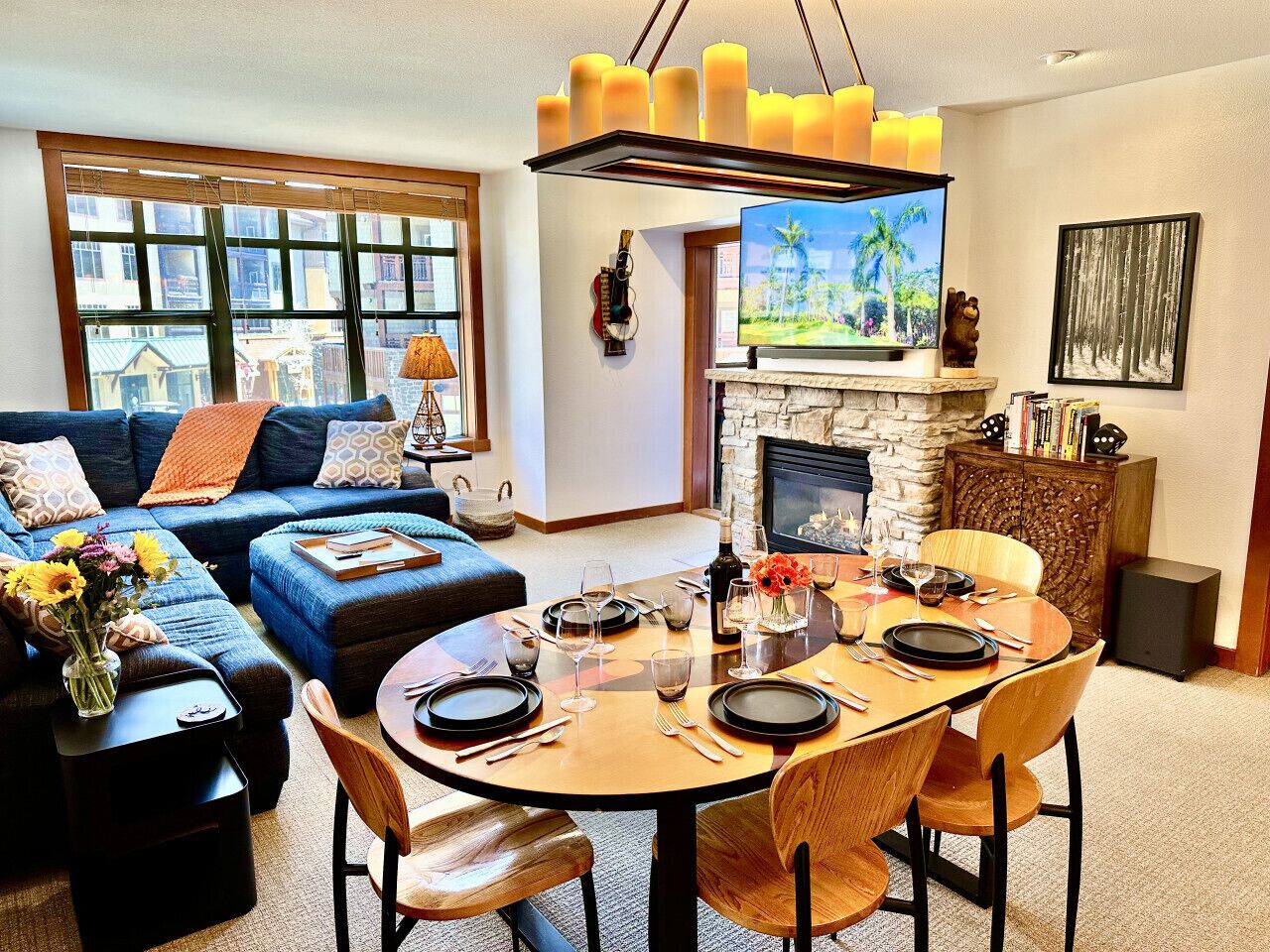 A living room with a fireplace, a dining table set for four, and a sofa with a view of the outside.