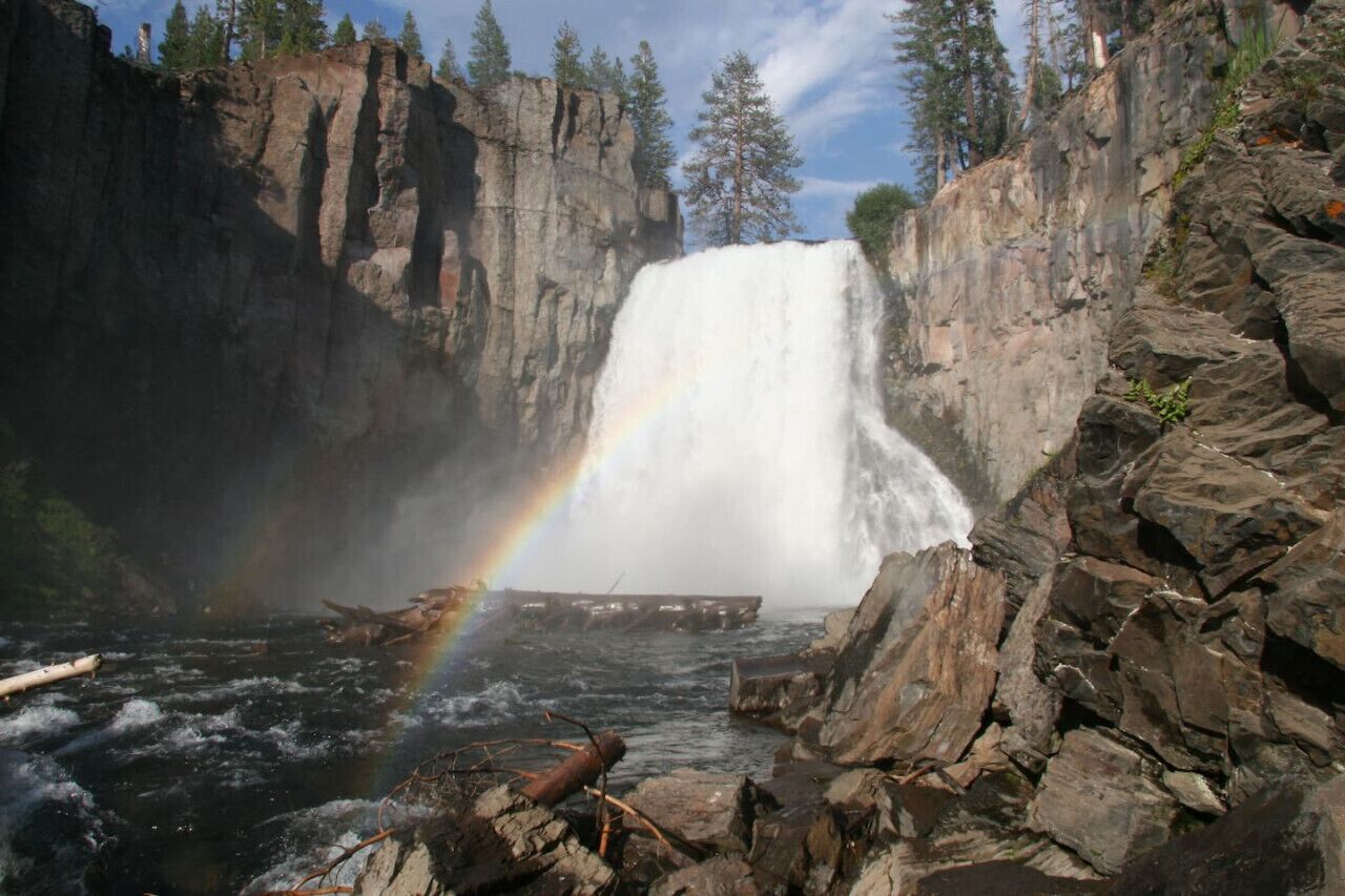 Een waterval met een regenboog, omringd door rotsachtige kliffen en bomen.