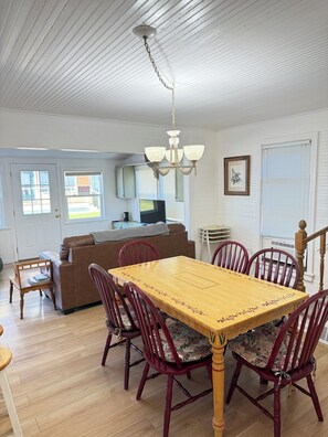 A dining area with a wooden table and chairs, a chandelier, a sofa, and a TV in the background.