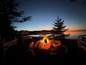 Un cadre paisible au bord du lac, avec un foyer, des chaises en bois et une jetée qui s’avance sur l’eau.