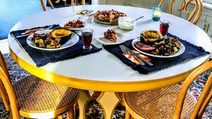 A dining table with plates of food, a glass of red drink, and a candle on a white tablecloth.