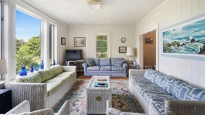 A cozy living room with wicker furniture, a television, and a painting of a seascape.