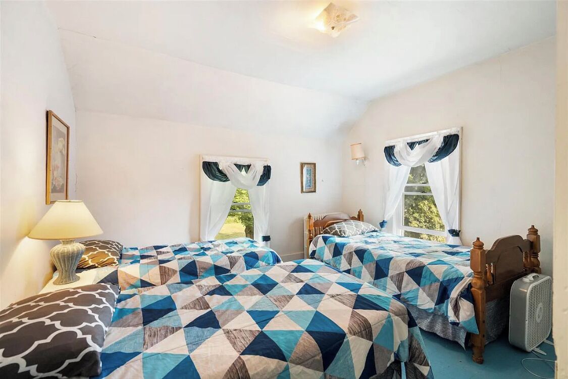 A bedroom with two beds, each with a geometric-patterned bedspread, a bedside table with a lamp, and a fan.