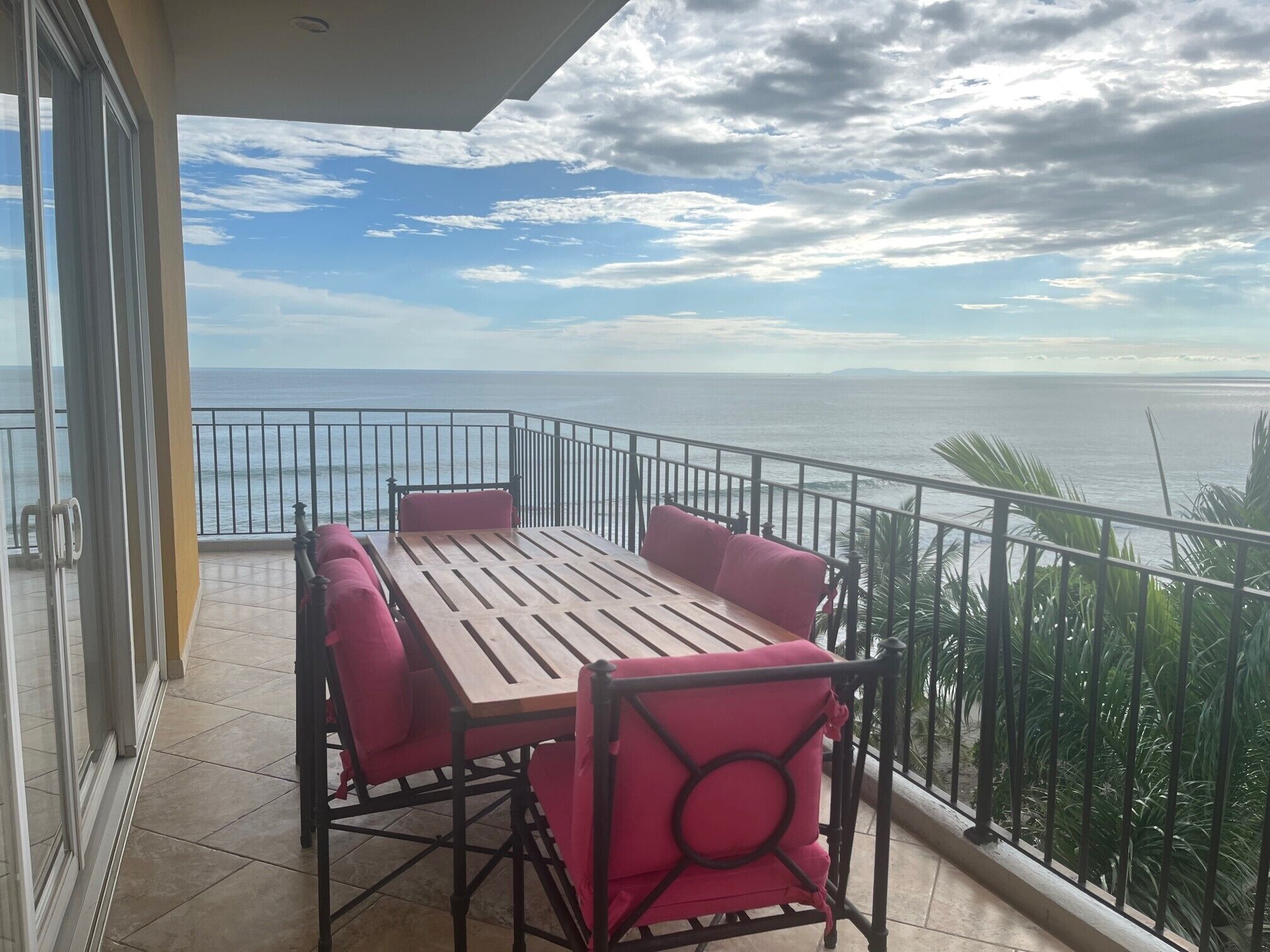 A balcony with a wooden table and four chairs, overlooking the sea.
