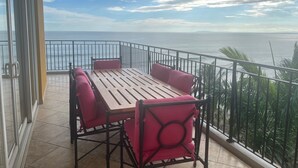 Un balcón con mesa de madera y cuatro sillas, con vista al mar.