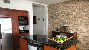 Una cocina con pared de piedra, armarios de madera, un refrigerador de acero inoxidable, un microondas y una estufa.