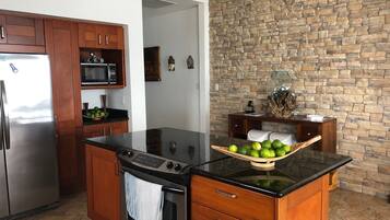 A kitchen with a stone wall, wooden cabinets, a stainless steel refrigerator, a microwave, and a stove.