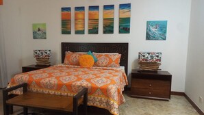 Un dormitorio con cama, mesitas de noche, una silla y obras de arte en las paredes.
