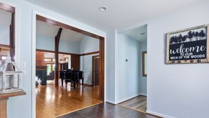 A spacious hallway with wooden flooring and a piano in the background. A welcome sign is displayed on the wall. - Breathtaking View with an Indoor Pool (bluemont)