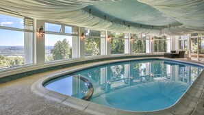 An indoor swimming pool with a view of the landscape through large windows, a ceiling draped with fabric, and a stone border around the pool. - Breathtaking View with an Indoor Pool (bluemont)