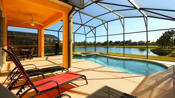 A covered outdoor area with a pool, lounge chairs, and a view of a lake. - FREE Pool/Spa heat - AMAZING  REVIEWS! Be My Guest!!  (Clermont)