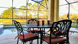 A patio with a round table and chairs, a pool, and a view of a golf course. - FREE Pool/Spa heat - AMAZING  REVIEWS! Be My Guest!!  (Clermont)