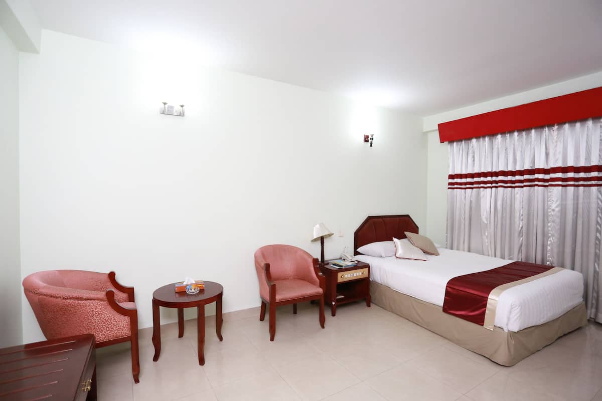A hotel room with a bed, two chairs, a nightstand, and a small table.