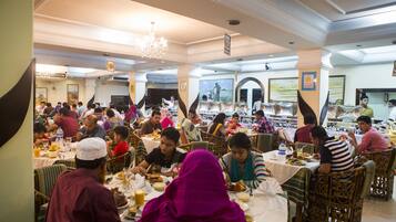 A crowded dining area with tables and chairs, people eating, and a chandelier.