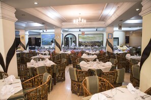 A restaurant with wicker chairs and tables, a chandelier, and a large painting on the wall. - Meridian Hotel (Chittagong)