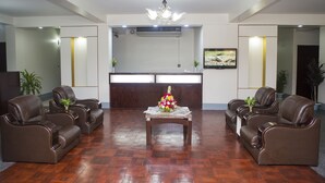 A reception area with a reception desk, two brown leather sofas, a coffee table with flowers, and a chandelier. - Meridian Hotel (Chittagong)