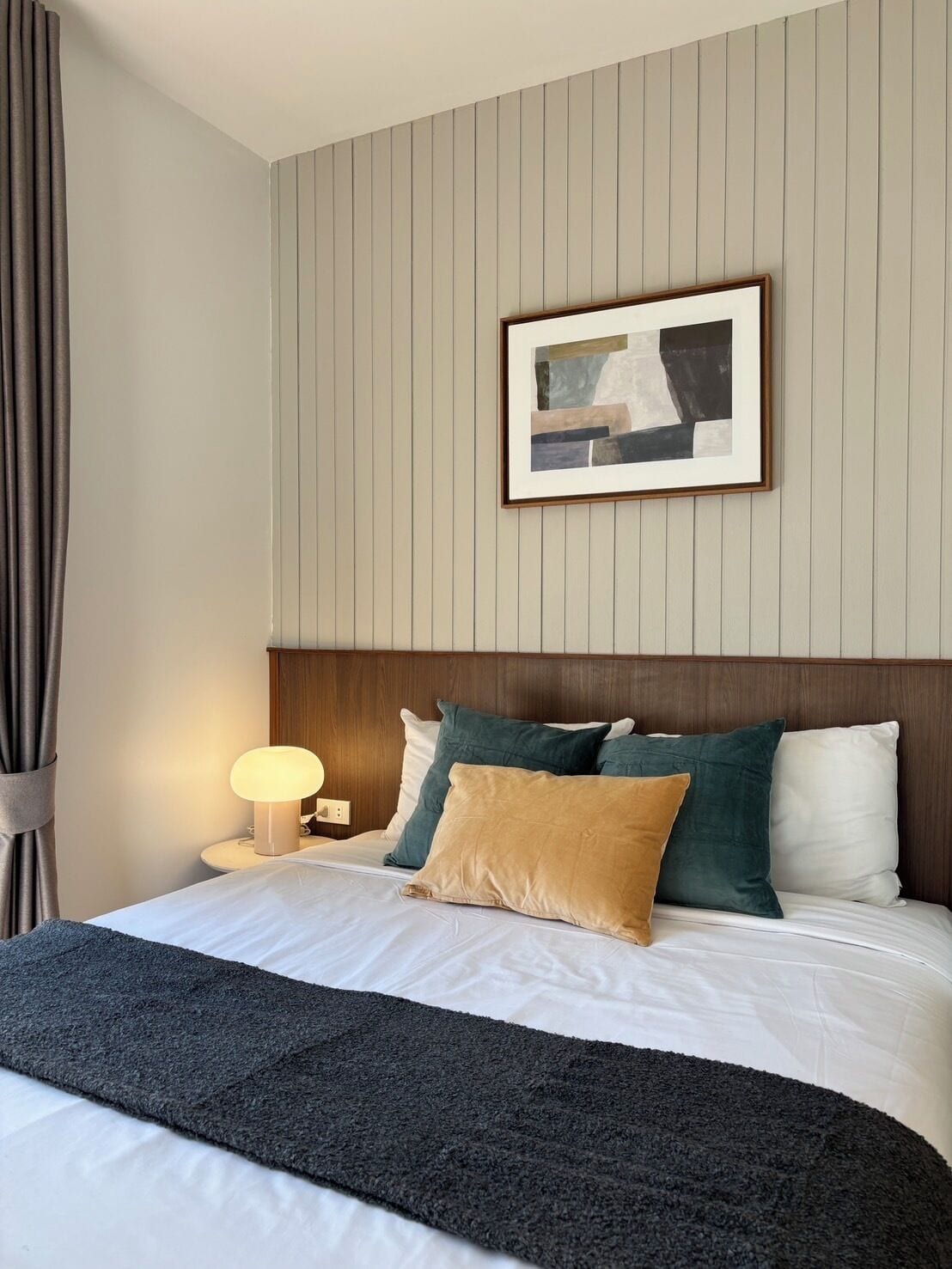 A hotel room with a bed, a headboard, a bedside lamp, a framed picture on the wall, and a curtain.