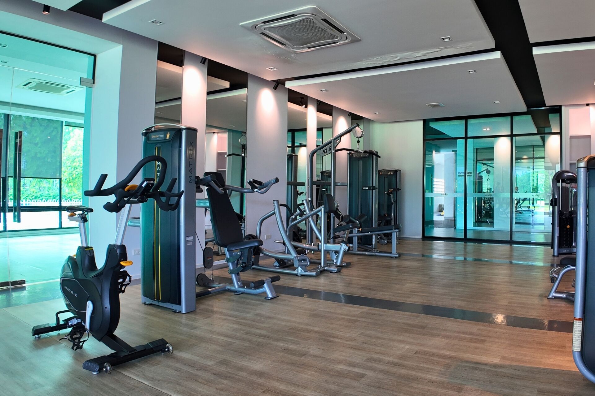 Un gimnasio moderno con diversos equipos de ejercicio, ventanas amplias y suelo de madera.
