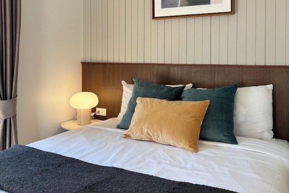 A hotel room with a bed, a nightstand, a lamp, a framed picture on the wall, and a window with curtains.