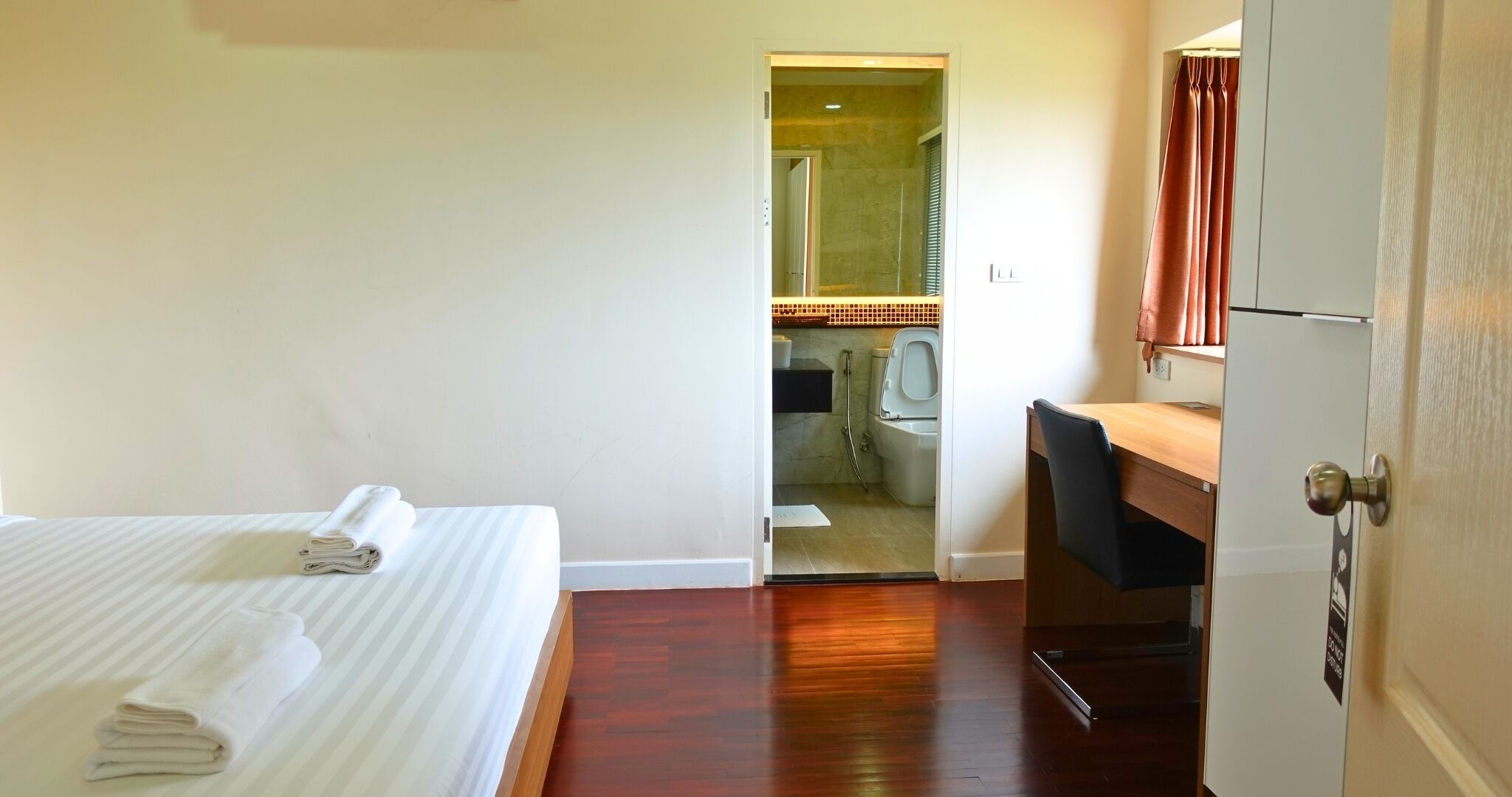 Ein Hotelzimmer mit Bett, Schreibtisch und einem durch eine offene Tür einsehbaren Badezimmer.
