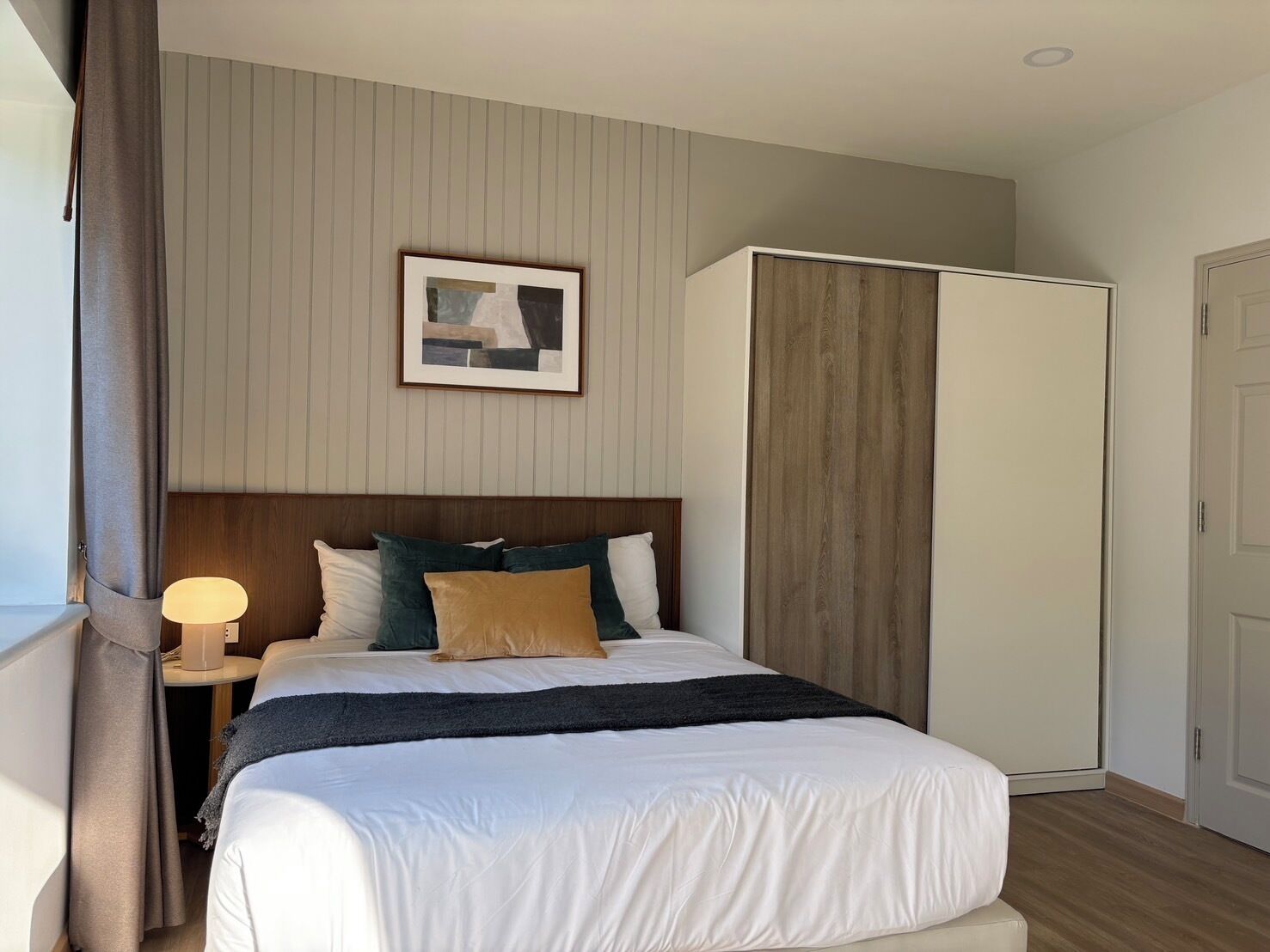 A neatly arranged bedroom with a bed, bedside lamp, and a framed picture on the wall.
