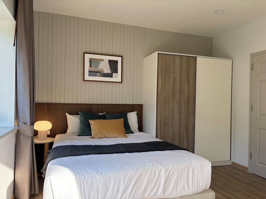 A neatly arranged bedroom with a bed, bedside lamp, and a framed picture on the wall.