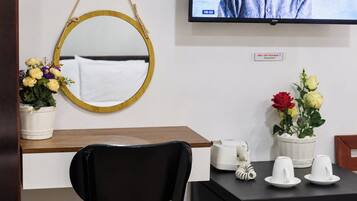 A hotel room with a wooden desk, a black chair, a round mirror, and two potted plants with flowers.