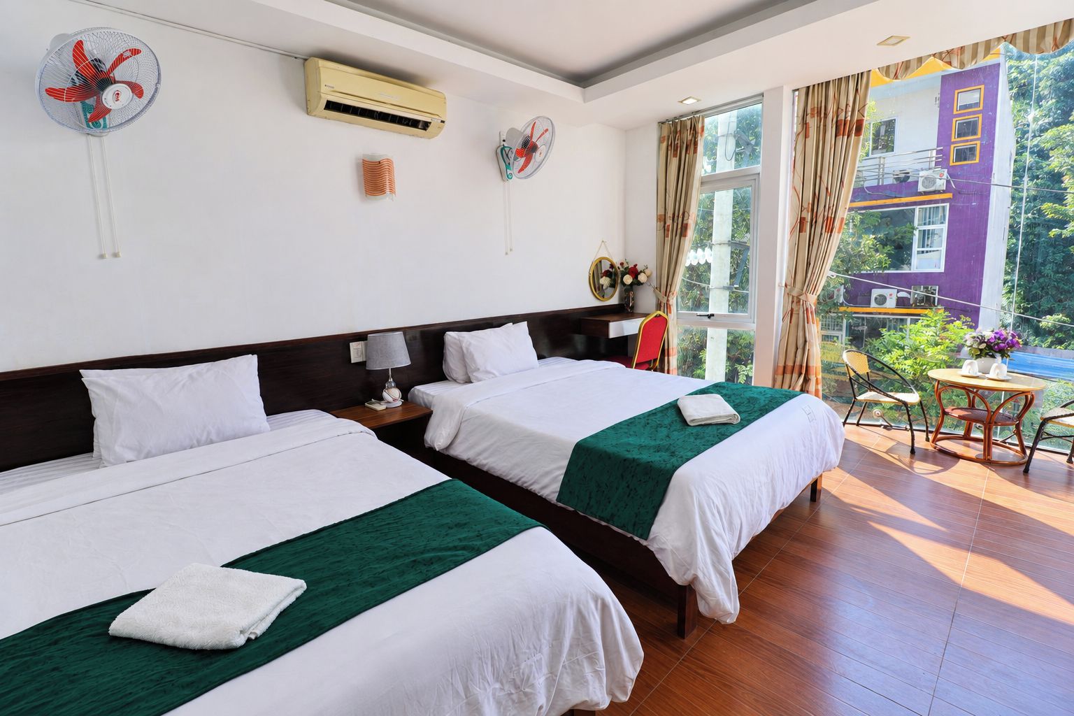 Ein Hotelzimmer mit zwei Betten, einem kleinen Tisch, Stühlen, einer Klimaanlage und Blick ins Freie.