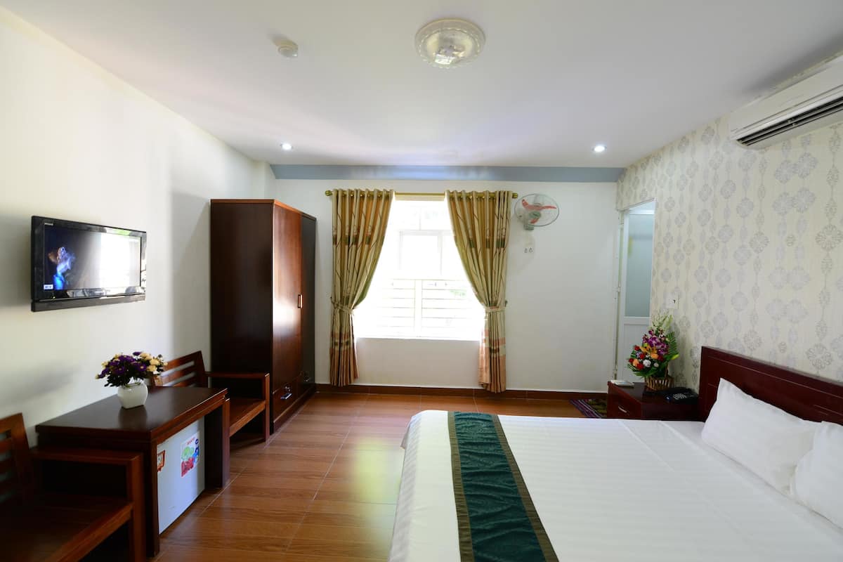 Hotelkamer met een bed, televisie, kledingkast, bureau met stoel en raam met gordijnen.