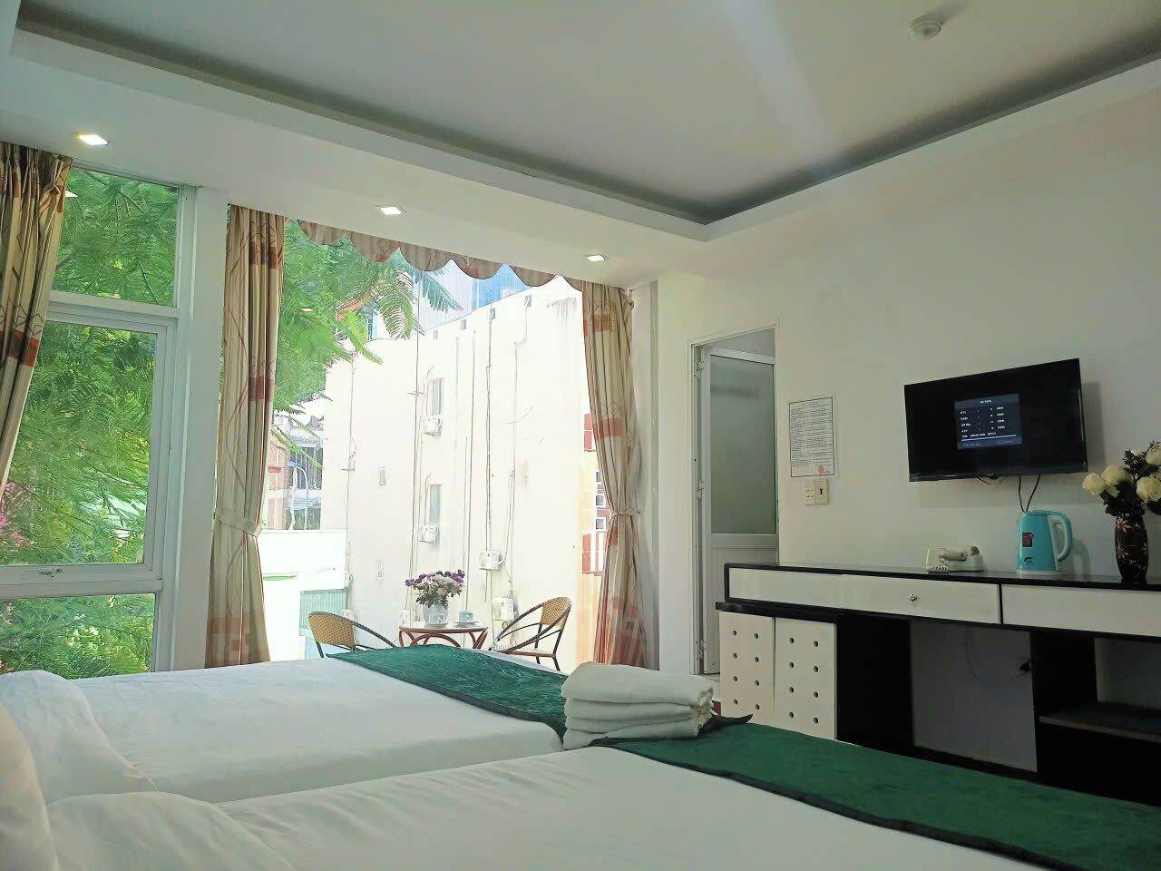 Habitación de hotel con dos camas, un escritorio con televisor, una ventana con cortinas y vista al exterior.