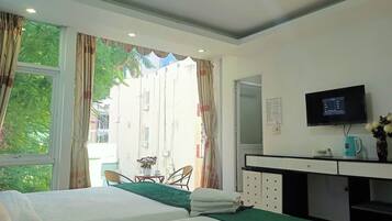 A hotel room with two beds, a desk with a TV, a window with curtains, and a view of the outside.