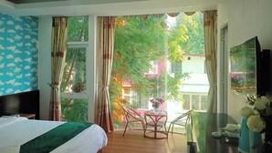 A hotel room with a bed, a desk, a chair, and a view of greenery outside. - Catba Island Hotel (Hai Phong)