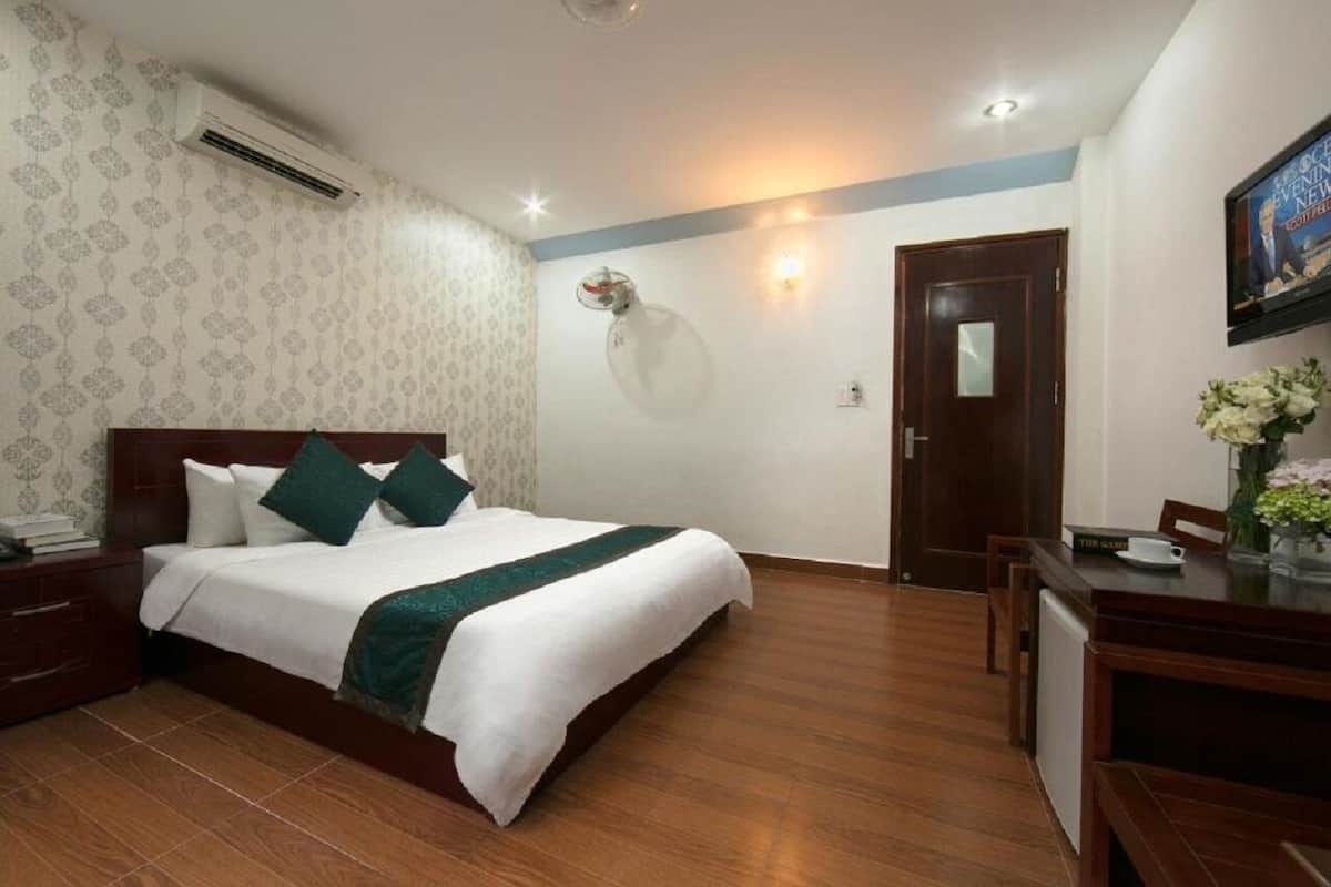 Een hotelkamer met een net opgemaakt bed, een houten nachtkastje, een bureau met stoel, en een aan de muur bevestigde televisie.