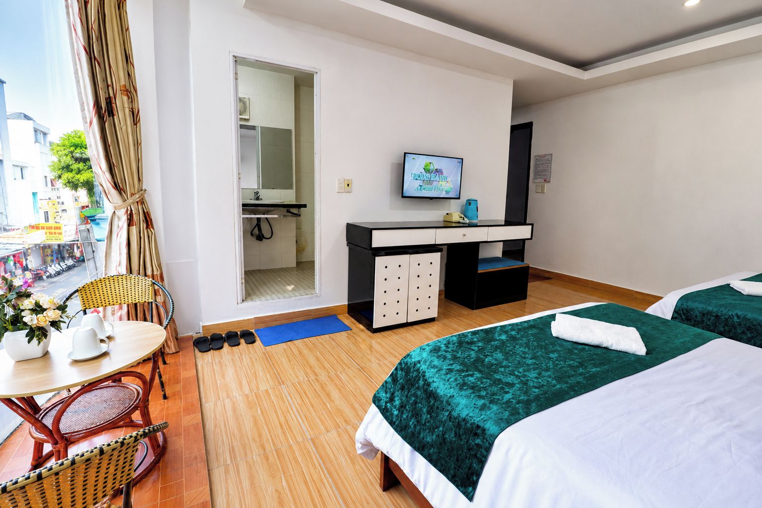A hotel room with two beds, a desk with a TV, a bathroom, and a view of the street.