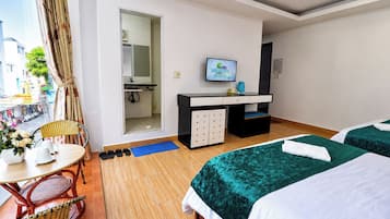 A hotel room with two beds, a desk with a TV, a bathroom, and a view of the street.