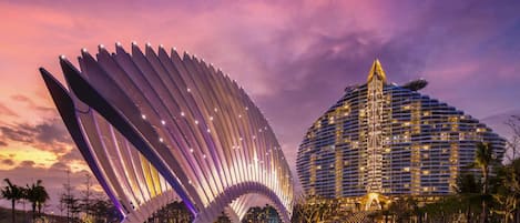Un hôtel moderne doté d’une façade incurvée originale et d’une structure en arc distinctive, illuminée, qui se détache au premier plan.