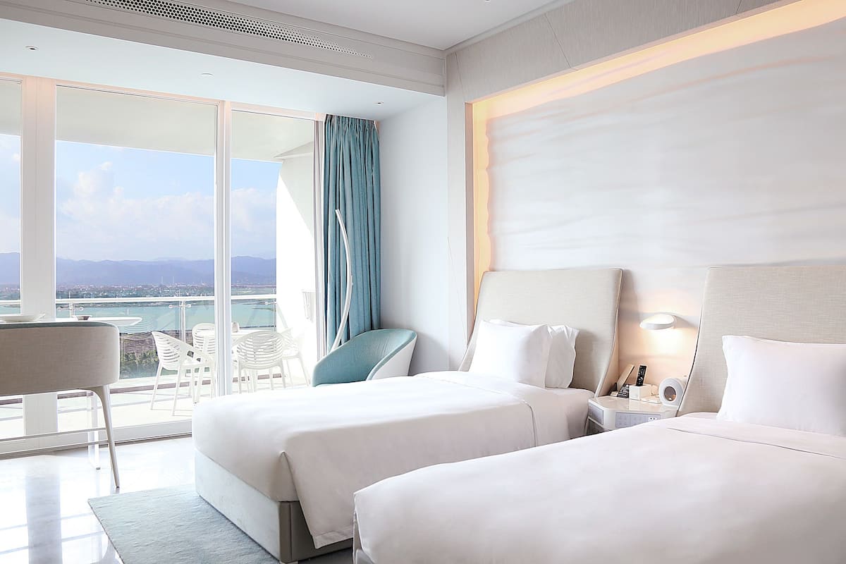 Habitación de hotel con dos camas, un balcón y vistas, una silla y una mesa.