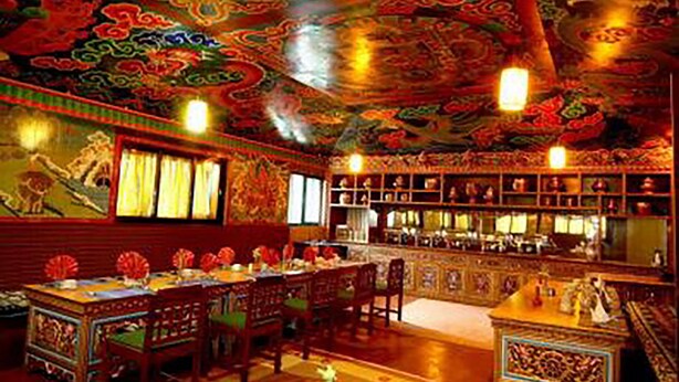 A traditional Chinese room with ornate red and gold decorations, a dining table set with dishes, and a bookshelf filled with books. - Mountain Lodges of Nepal - Thame (Thame)