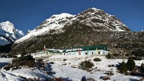 A mountain lodge with a green roof, surrounded by snow-covered terrain and mountains. - Mountain Lodges of Nepal - Thame (Thame)