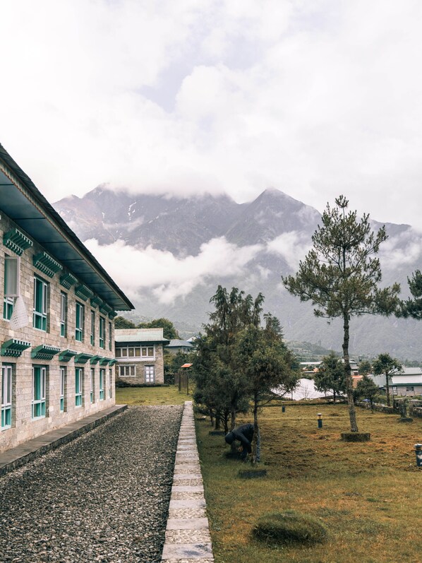 A traditional building with a stone facade and green window frames, a paved pathway, and a grassy area with trees.
