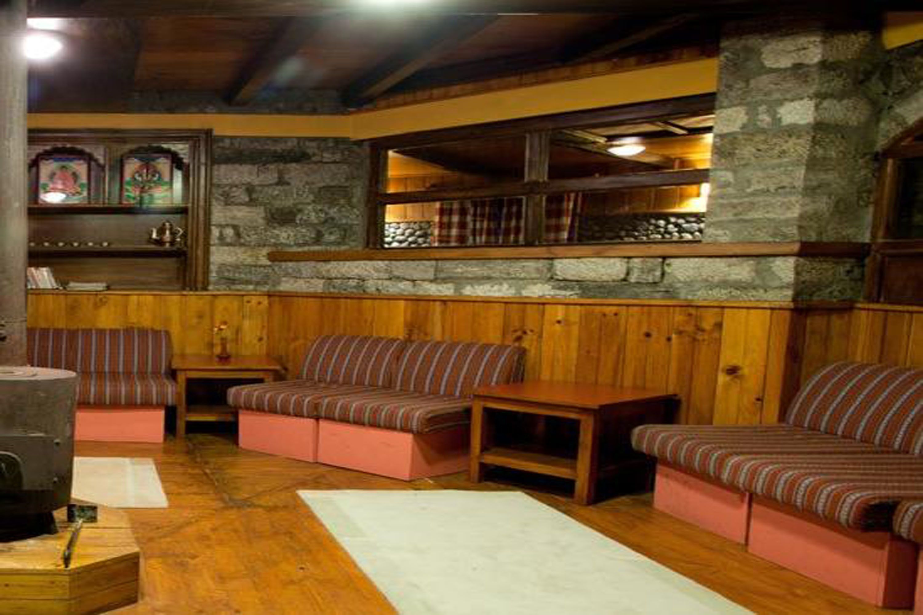 Una habitación acogedora con paredes de madera y una chimenea de piedra. Hay bancos acolchados y una pequeña mesa.