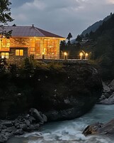 Un edificio de piedra con techo rojo, ubicado junto a un río y un saliente rocoso al frente.