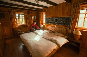 Una habitación de madera con una cama grande, una silla, una chimenea y una ventana con cortinas.