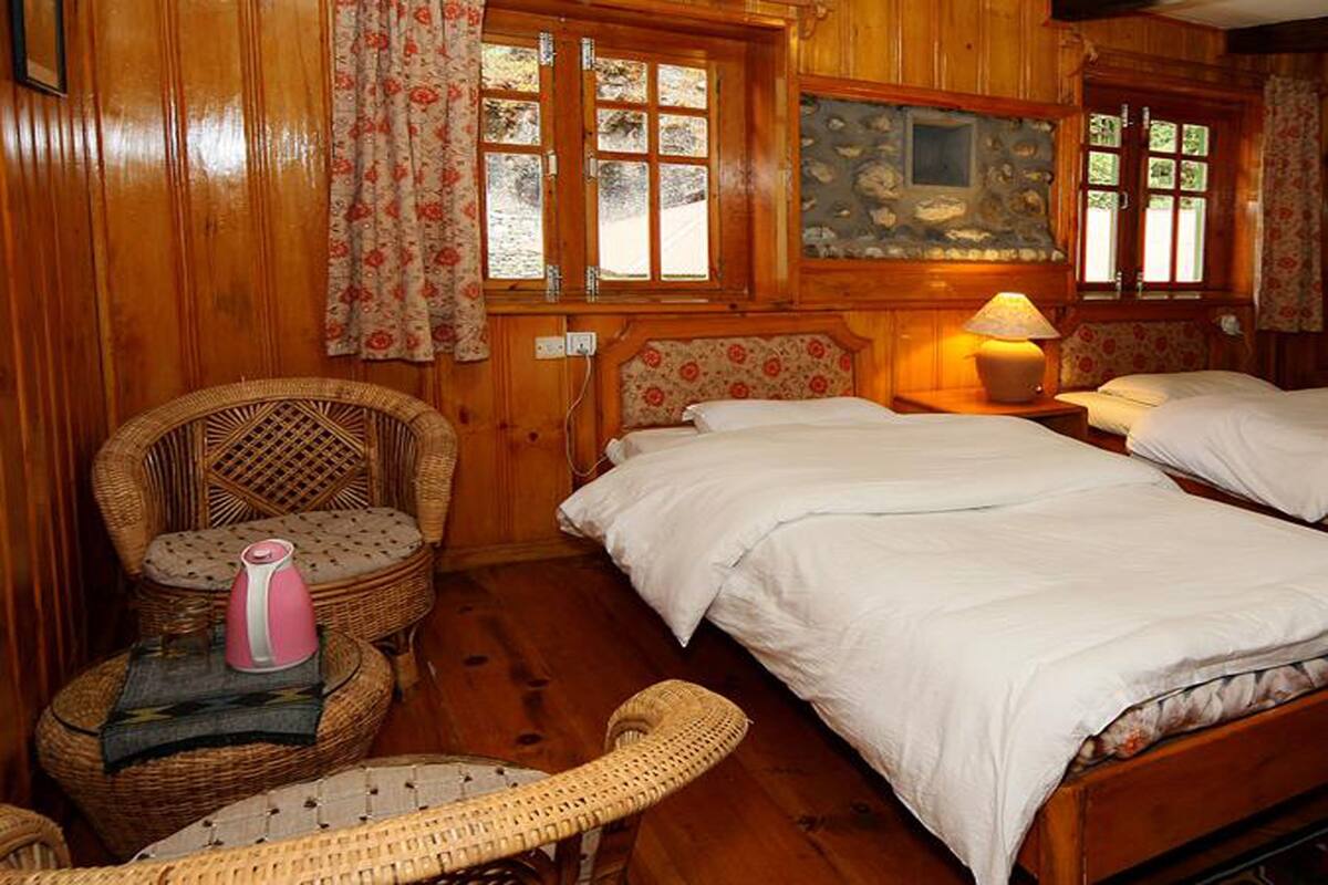 A wooden room with two beds, a wicker chair, a table with a lamp, and a window with curtains.