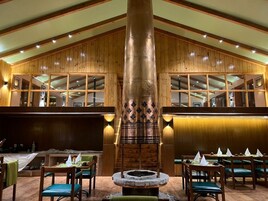 Un restaurante con paneles de madera, una chimenea central y varias mesas con sillas.