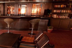 Un área de bar con un mostrador de madera, dos taburetes y una estantería llena de libros.